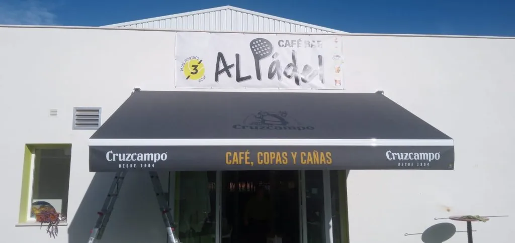 Toldo con lona negra y faldilla rotulada en un negocio