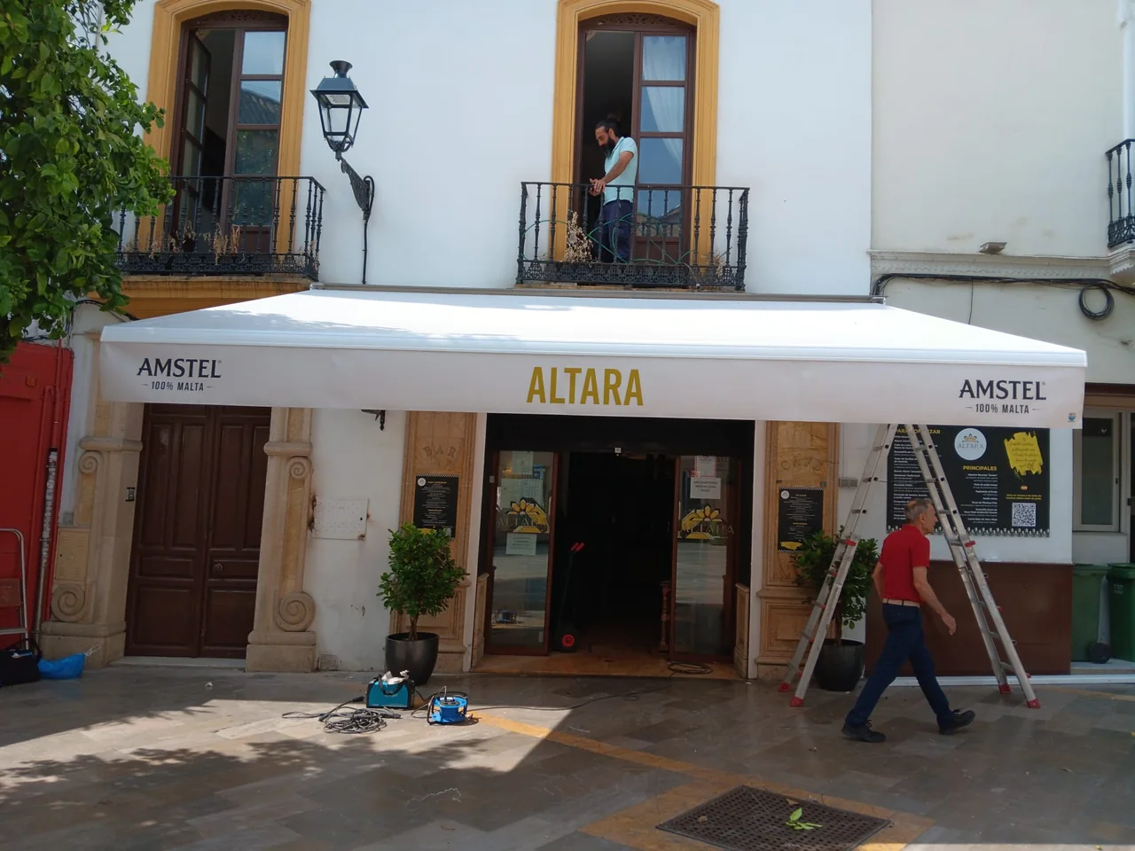 Toldo blanco de Bar Altara en Sevilla, con el nombre del bar en dorado y los logotipos de Amstel en la faldilla