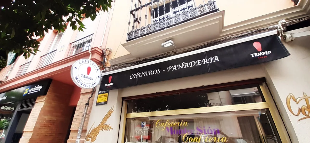 Toldo negro en la calle Feria de Sevilla, con marcas Templo Cafés y el texto Churros - Panadería en blanco